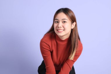 Mor arka planda dikilen, günlük giysiler içindeki genç Güneydoğu Asyalı kadın..