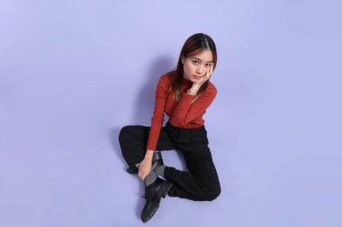 Mor arka planda dikilen, günlük giysiler içindeki genç Güneydoğu Asyalı kadın..