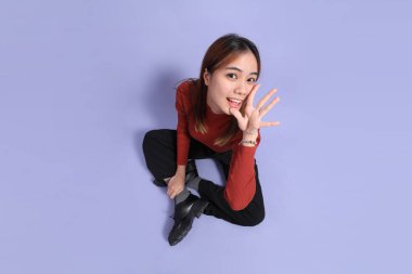 Mor arka planda dikilen, günlük giysiler içindeki genç Güneydoğu Asyalı kadın..