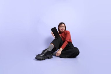 Mor arka planda dikilen, günlük giysiler içindeki genç Güneydoğu Asyalı kadın..