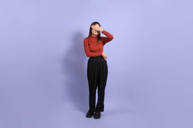 Mor arka planda dikilen, günlük giysiler içindeki genç Güneydoğu Asyalı kadın..