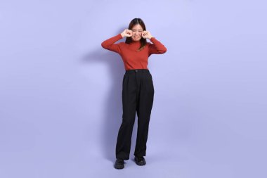 Mor arka planda dikilen, günlük giysiler içindeki genç Güneydoğu Asyalı kadın..