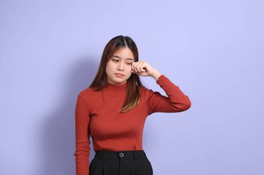 Mor arka planda dikilen, günlük giysiler içindeki genç Güneydoğu Asyalı kadın..