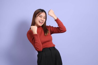 Mor arka planda dikilen, günlük giysiler içindeki genç Güneydoğu Asyalı kadın..