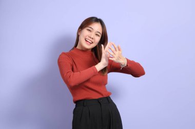 Mor arka planda dikilen, günlük giysiler içindeki genç Güneydoğu Asyalı kadın..