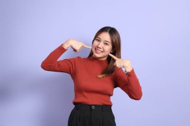 Mor arka planda dikilen, günlük giysiler içindeki genç Güneydoğu Asyalı kadın..