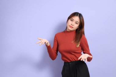 Mor arka planda dikilen, günlük giysiler içindeki genç Güneydoğu Asyalı kadın..