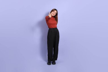 Mor arka planda dikilen, günlük giysiler içindeki genç Güneydoğu Asyalı kadın..