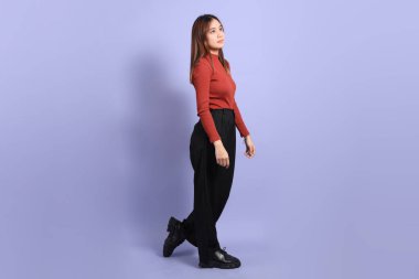 Mor arka planda dikilen, günlük giysiler içindeki genç Güneydoğu Asyalı kadın..