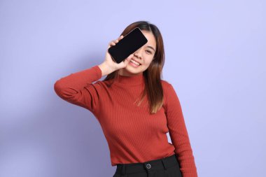 Mor arka planda dikilen, günlük giysiler içindeki genç Güneydoğu Asyalı kadın..