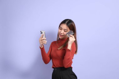 The young Southeast Asian woman in casual clothes, standing against a purple background.