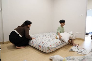 Güneydoğu Asyalı bekar bir anne, oğlunun yatak odasındaki çarşafları değiştirmesine yardım ediyor..