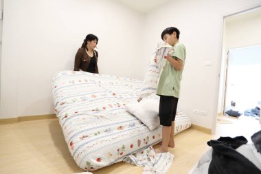 Güneydoğu Asyalı bekar bir anne, oğlunun yatak odasındaki çarşafları değiştirmesine yardım ediyor..