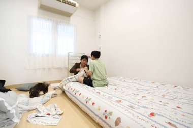 Güneydoğu Asyalı bekar bir anne, oğlunun yatak odasındaki çarşafları değiştirmesine yardım ediyor..