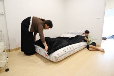 Güneydoğu Asyalı bekar bir anne, oğlunun yatak odasındaki çarşafları değiştirmesine yardım ediyor..