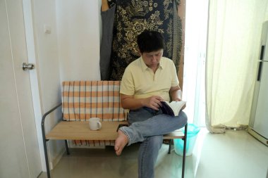 Doğu Asyalı adam bankta oturuyor ve evde kitap okuyor..