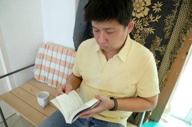 Doğu Asyalı adam bankta oturuyor ve evde kitap okuyor..