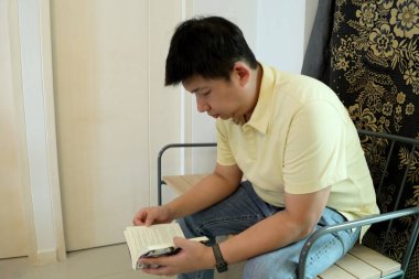 Doğu Asyalı adam bankta oturuyor ve evde kitap okuyor..