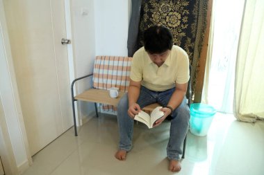 Doğu Asyalı adam bankta oturuyor ve evde kitap okuyor..