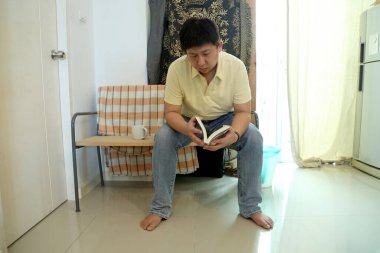 Doğu Asyalı adam bankta oturuyor ve evde kitap okuyor..