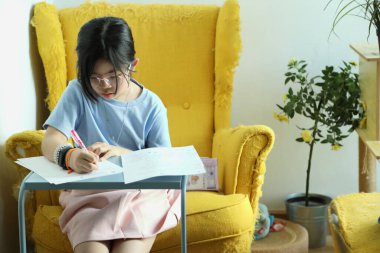 Doğu Asyalı kız evinde koltukta ödev yapıyor..