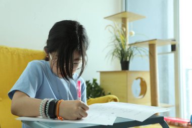 Doğu Asyalı kız evinde koltukta ödev yapıyor..