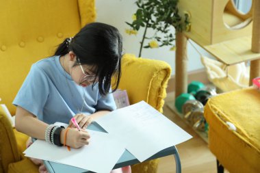 Doğu Asyalı kız evinde koltukta ödev yapıyor..