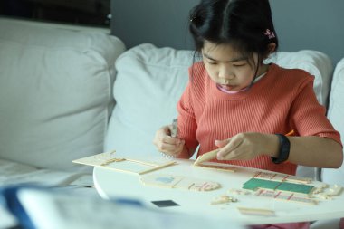 Doğu Asyalı bir kız oturma odasında ahşap bir model ev kuruyor..