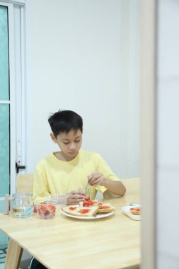 Güneydoğu Asyalı çocuk çilekli sandviç yapıyor ve evde tek başına yiyor..