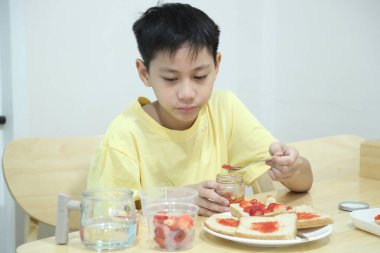 Güneydoğu Asyalı çocuk çilekli sandviç yapıyor ve evde tek başına yiyor..