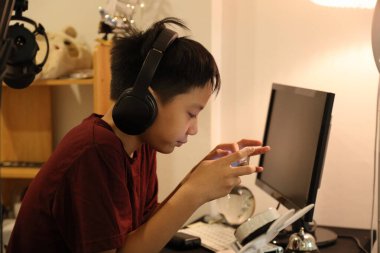 Güneydoğu Asyalı çocuk bilgisayar masasında akıllı telefonuyla oyun oynuyor..