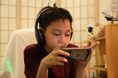 Güneydoğu Asyalı çocuk bilgisayar masasında akıllı telefonuyla oyun oynuyor..