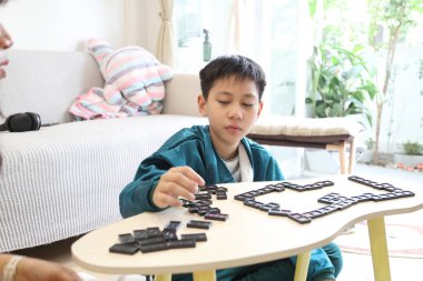 Güneydoğu Asyalı çocuk annesiyle oturma odasında domino oynuyor..