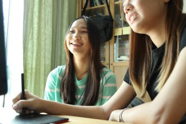 Güneydoğu Asyalı genç kız kardeşiyle bilgisayardan yeni yazılımlar öğreniyor..