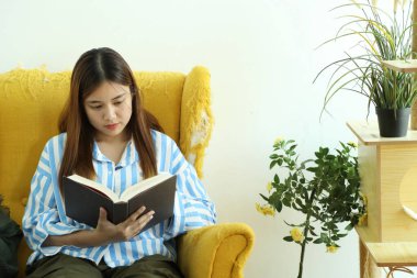 Güneydoğu Asyalı kadın dinleniyor ve koltukta kitap okuyor..