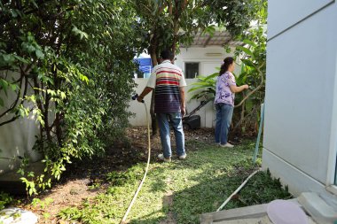 Doğu Asyalı yaşlı çift evin etrafındaki bahçedeki çiçekleri suluyor..