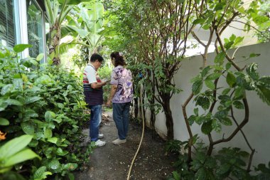 Doğu Asyalı yaşlı çift evin etrafındaki bahçedeki çiçekleri suluyor..