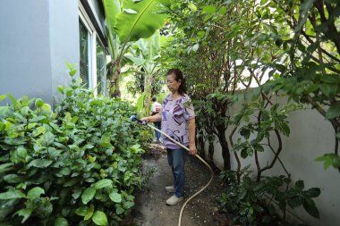 Doğu Asyalı yaşlı çift evin etrafındaki bahçedeki çiçekleri suluyor..