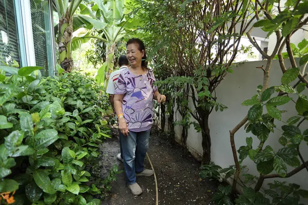 Doğu Asyalı yaşlı çift evin etrafındaki bahçedeki çiçekleri suluyor..