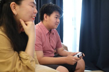 Güneydoğu Asya 'lı bekar anne, genç oğlunun televizyonda oyun oynamasını izliyor..