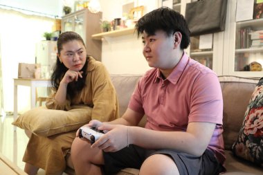 Güneydoğu Asya 'lı bekar anne, genç oğlunun televizyonda oyun oynamasını izliyor..