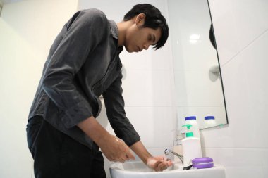 Güneydoğu Asyalı adam yüzünü yıkıyor ve saçını banyoda şekillendiriyor..