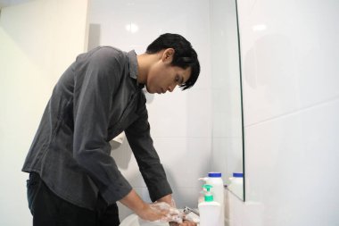 Güneydoğu Asyalı adam yüzünü yıkıyor ve saçını banyoda şekillendiriyor..