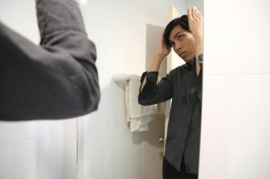 Güneydoğu Asyalı adam yüzünü yıkıyor ve saçını banyoda şekillendiriyor..