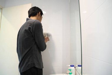 Güneydoğu Asyalı adam yüzünü yıkıyor ve saçını banyoda şekillendiriyor..