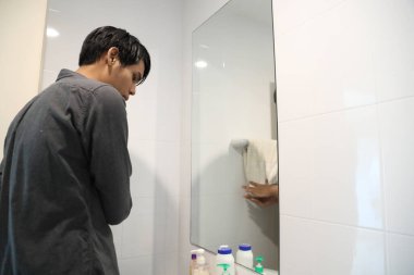 Güneydoğu Asyalı adam yüzünü yıkıyor ve saçını banyoda şekillendiriyor..