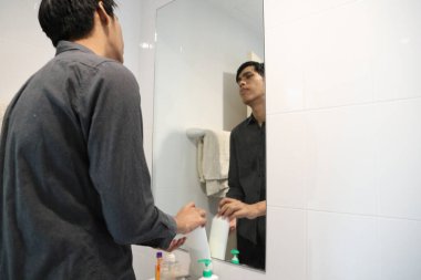 Güneydoğu Asyalı adam yüzünü yıkıyor ve saçını banyoda şekillendiriyor..