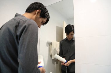 Güneydoğu Asyalı adam yüzünü yıkıyor ve saçını banyoda şekillendiriyor..