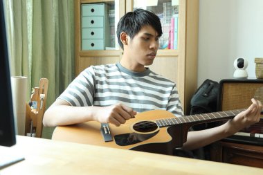 Güneydoğu Asyalı adam ilk defa internetten gitar çalmayı öğreniyor.