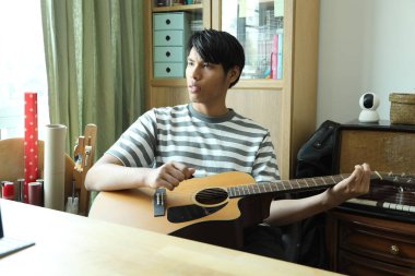 Güneydoğu Asyalı adam ilk defa internetten gitar çalmayı öğreniyor.